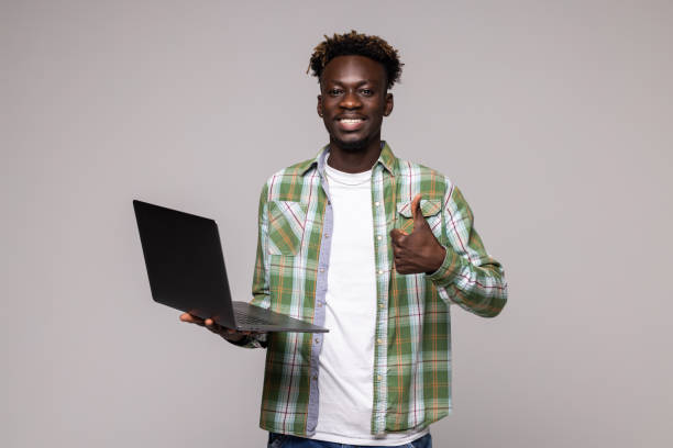 istock Young smiling african man standing and using laptop computer over gray background 1341619121