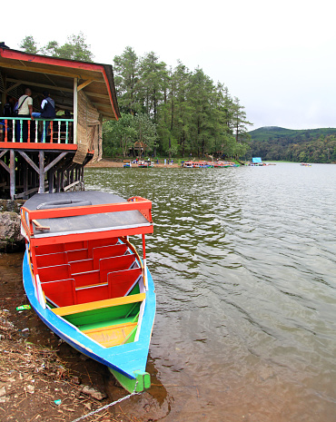 Lakeside view with a colorful boat and people at a restaurant at Lake Patenggang in Ciwidey, West Java, Indonesia.