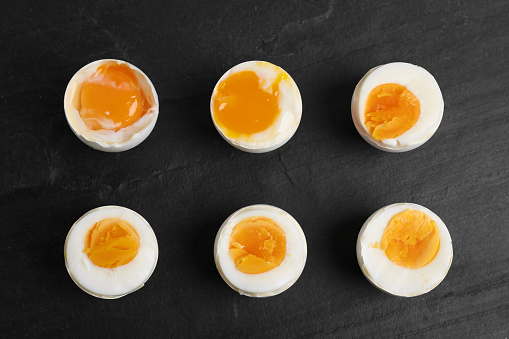 Different readiness stages of boiled chicken eggs on black table, flat lay