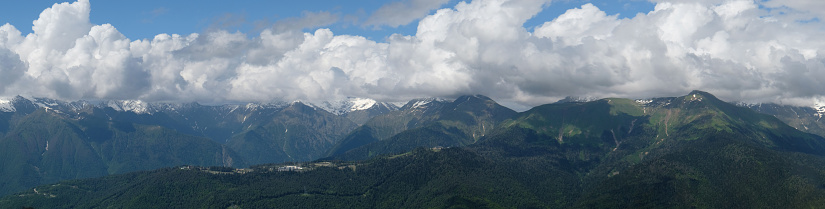 View of green mountains with snowy peaks. Blue sky and clouds cover the mountain peak. Traveling and resting in the mountains in summer, hiking, climbing the mountain. Mountain landscape.