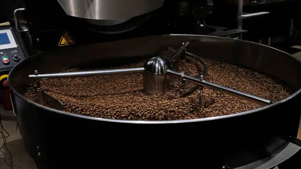 Photo of Coffee roaster machine at coffee roasting process. Mixing coffee beans. Roasted spinning cooler professional machines and fresh brown coffee beans movement close-up dark photo at factory.