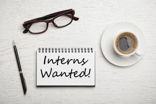 istock Notepad with text INTERNS WANTED, coffee, glasses and pen on white wooden table, flat lay 1341624133