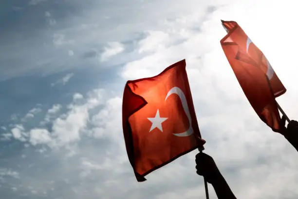 Photo of Two Hands holding Turkish flags on a blue and cloudy sky and on the day of liberty Izmir.