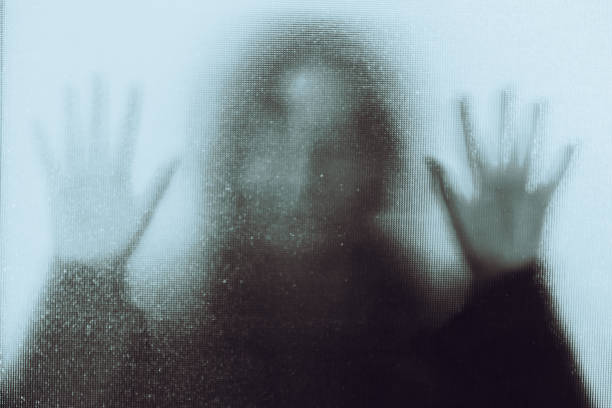 Domestic abuse victim with hands pressed against glass window Back lit image of the silhouette of a woman with her hands pressed against a glass window. The silhouette is distorted, and the arms elongated, giving an alien-like quality. The image is sinister and foreboding, with an element of horror. It is as if the 'woman' is trying to escape from behind the glass. ghost stock pictures, royalty-free photos & images