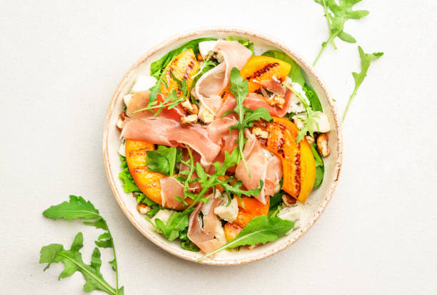 istock Salad bowl with grilled peach, prosciutto, goat cheese, walnuts and arugula on white background, top view, copy space 1341626158