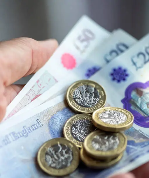 A man's hand holding £50 and £20 pound notes and pound coins