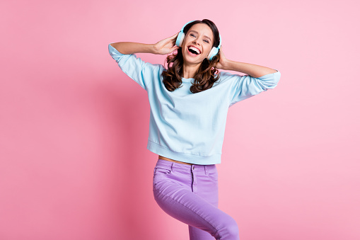 Photo of young girl happy smile have fun crazy listen music earphones wear violet trousers isolated over pink color background.