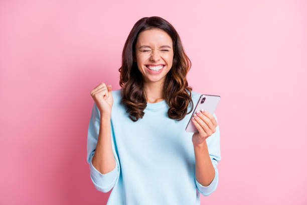 foto de joven loca emocionada puños de mano celebran ganar victoria éxito usar teléfono celular aislado sobre fondo de color rosa - eufórico fotografías e imágenes de stock