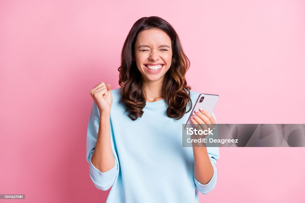 Photo of young excited crazy girl fists hand celebrate win victory success use cellphone isolated over pink color background Photo of young excited crazy girl fists hand celebrate win victory success use cellphone isolated over pink color background. One Woman Only Stock Photo
