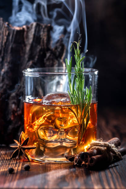 Halloween drinks. Whiskey, rum, or bourbon poured into a transparent skull-shaped glass. Halloween drinks. Whiskey, rum, or bourbon poured into a transparent skull-shaped glass. Mystical setting and smoke around. Close-up. glass of bourbon stock pictures, royalty-free photos & images
