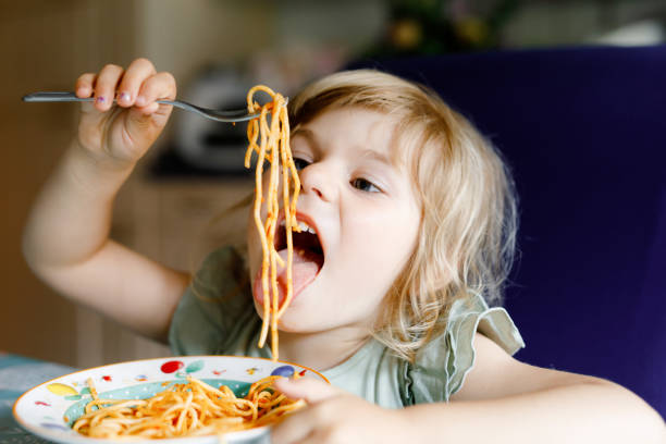 entzückendes kleinkind mädchen essen pasta spaghetti mit tomaten bolognese mit hackfleisch. glückliches vorschulkind, das frisch gekochte gesunde mahlzeit mit nudeln und gemüse zu hause und drinnen isst. - essen mund benutzen stock-fotos und bilder