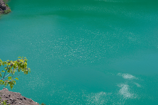 Background from emerald green water saturated with radon. Flooded granite quarry, tree leaves.