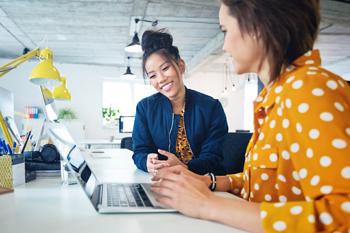 Smiling female businesswomen working together in new office. Two creative women are sitting at workplace. They are in casuals.