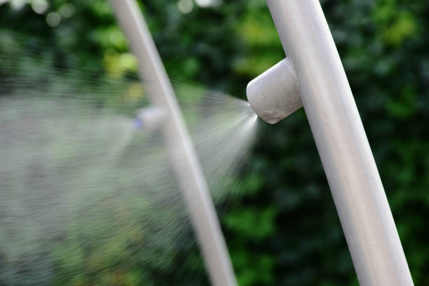 fine water spray or mist nozzle. restaurant terrace cooling and vaporizing. outdoor summer cooling. aluminum pipe. blurred green foliage background. summer vacation concept. misting system