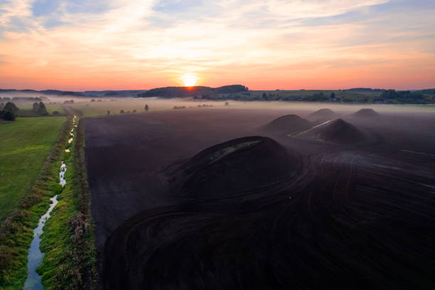 Peat extraction site in fog on sunset. Collecting peat on peatlands. Mining and harvesting peatland. Area drained of the mire are used for peat extraction. Drainage and destruction of peat bogs.