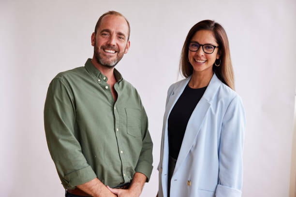 Two businesspeople smiling together against a white background Portrait of two businesspeople smiling while standing side by side together in front of a white background side by side stock pictures, royalty-free photos & images