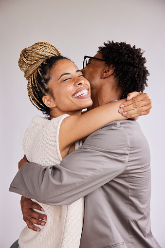 Laughing young African American woman hugging her boyfriend with her eyes closed in front of a white background