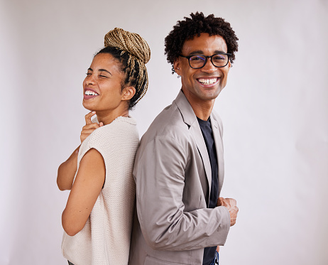 Portrait of two young African American businesspeople standing back to back together in front of a white background and laughing