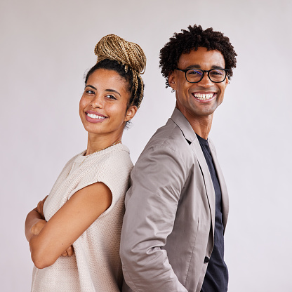 Portrait of two young African American businesspeople standing back to back together in front of a white background and smiling