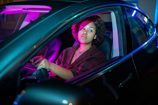 Young African-American woman driving electric car while holding by steering wheel