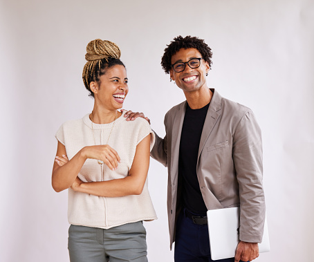 Two young African American businesspeople standing together and laughing in front of a white background