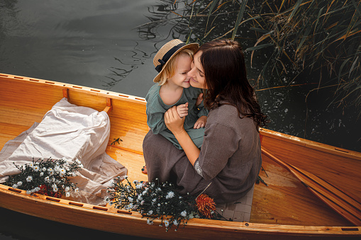 Beautiful happy family, mother and daughter in a wooden boat decorated with flowers on the lake together.