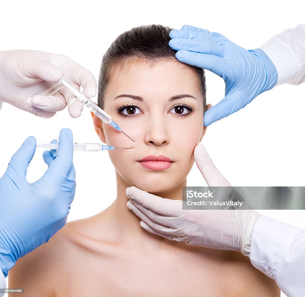 Woman having botox into face Plastic surgeons giving injection of botox into face - isolated white Adult Stock Photo