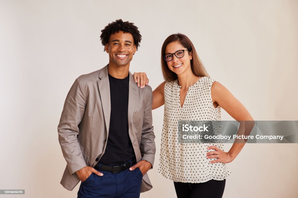 Diverse young businesspeople standing on a white background and smiling Portrait of two diverse young businesspeople smiling confidently while standing side by side together on a light background Two People Stock Photo