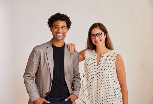 Portrait of two diverse young businesspeople standing side by side and smiling in front of a white background