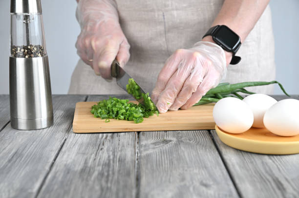 A woman in gloves slices green onions with a large kitchen knife