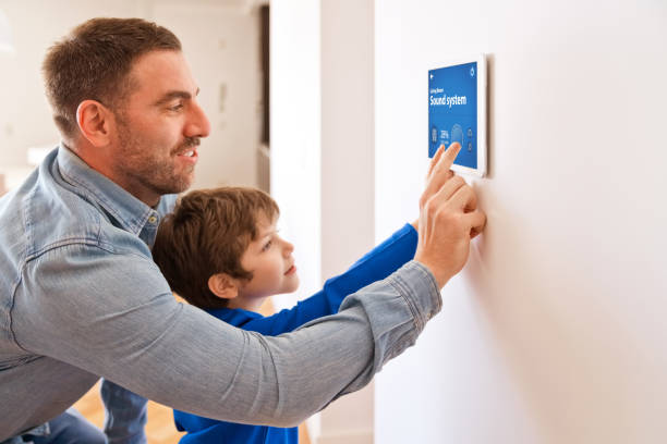 Father with son controlling smart devices with a digital tablet at home Father teaching his son controlling home with a digital touch screen panel. Concept of internet of things. smart home family stock pictures, royalty-free photos & images