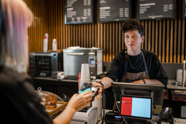 Smiling Barista taking Fast and easy payment in the coffee shop Smiling Barista taking Fast and easy payment in the coffee shop lgbtqcollection stock pictures, royalty-free photos & images