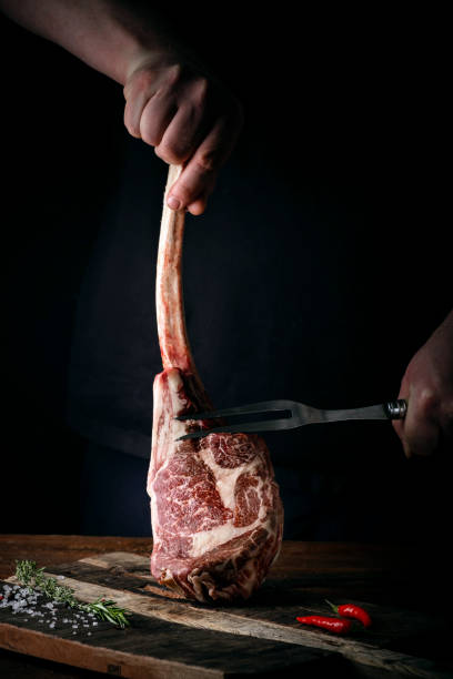 istock The chef's hands hold a raw Tomahawk a beef steak and a meat fork over a chopping Board 1341649062