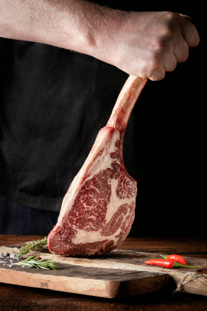 istock A man holds a Raw Tomahawk steak on a bone of dry aged beef on a dark background 1341649096