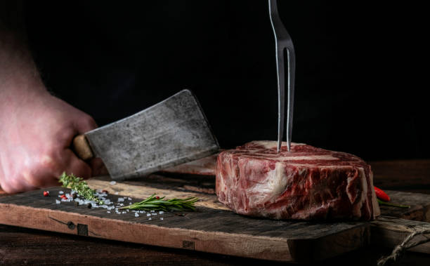 istock A butcher cuts beef Tomahawk steak on a bone with a cleaver on a wooden cutting Board on a dark background 1341649117