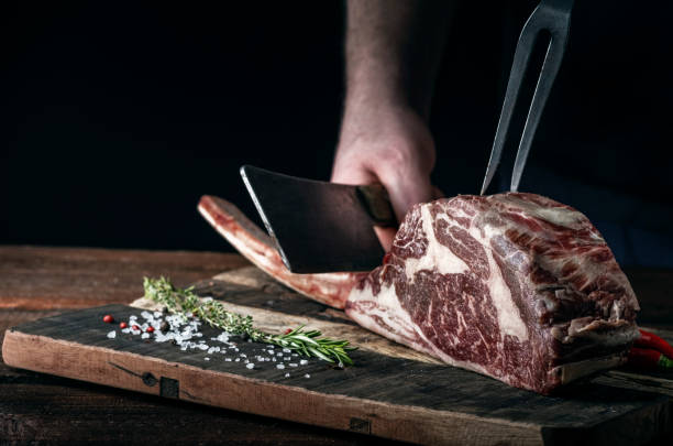 istock A butcher cuts beef Tomahawk steak on a bone with a cleaver on a wooden cutting Board on a dark background 1341649131