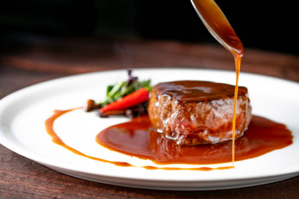 grilled beef tenderloin steak on a white platter is served with demiglas sauce - close up roasted meal pepper imagens e fotografias de stock