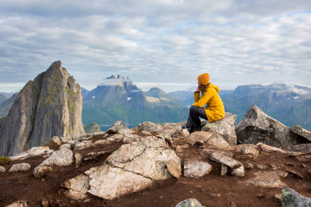 kobieta w żółtym płaszczu przeciwdeszczowym, siedząca tyłem na skale i patrząca na górę segla na wyspie senja w północnej norwegii. niesamowity piękny krajobraz i wspaniała przyroda w skandynawskim kraju - mountain climbing rock climbing motivation awe zdjęcia i obrazy z banku zdjęć
