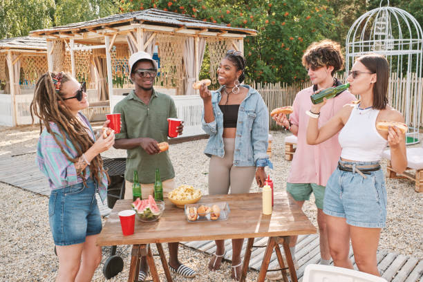 Young friends having hotdogs and drinks outdoors Young friends having hotdogs and drinks outdoors while enjoying summer weekend black man eating watermelon stock pictures, royalty-free photos & images