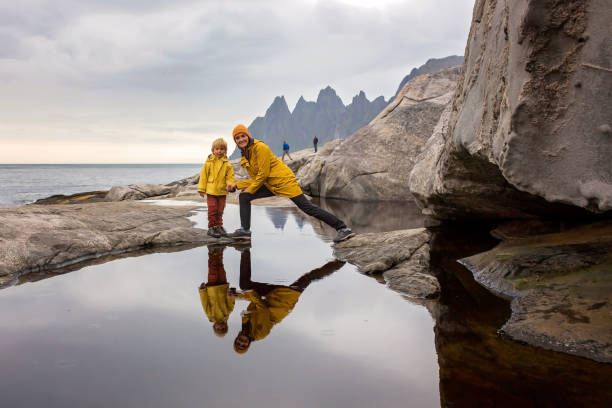 mulher, se divertindo com a criança em tungeneset, senja, noruega, pulando sobre uma grande poça, deixando reflexo na água - beach family boardwalk footpath - fotografias e filmes do acervo