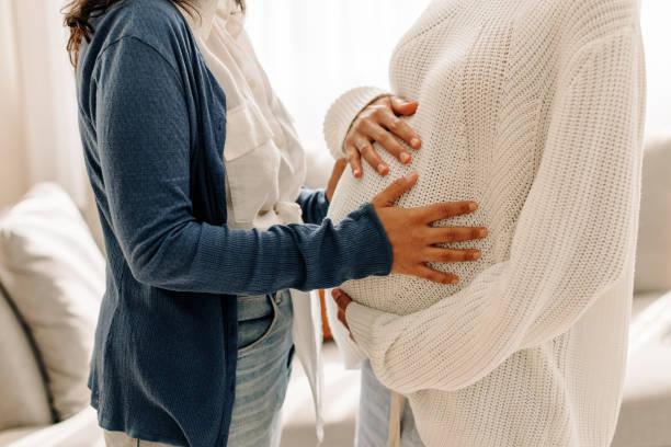 Unrecognizable young woman touching her surrogate's pregnant bel Unrecognizable young woman touching a surrogate mother's belly bump. Young woman spending time with her surrogate at home. Woman feeling the movement of a pregnant woman's baby. surrogacy stock pictures, royalty-free photos & images