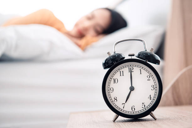 istock Young woman sleeping on bed with alarm clock in morning. 1341652213