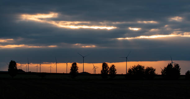 silhouette d’éoliennes et d’arbres à l’horizon au coucher du soleil. spectaculaire ciel orange brillant avec des nuages. - dramatic sky dusk night sustainable resources photos et images de collection