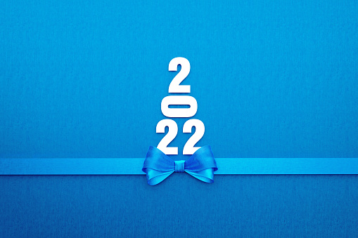 2022 text forming a Christmas tree and is tied with blue ribbon on blue background. Horizontal composition with copy space. Directly above. Great use for Christmas and 2022 concepts.