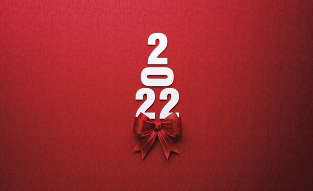 2022 text forming a Christmas tree and is tied with red ribbon on red background. Horizontal composition with copy space. Directly above. Great use for Christmas and 2022 concepts.