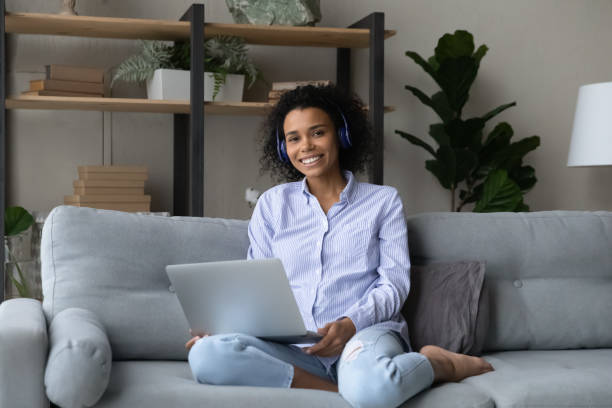 istock Smiling african female in headset sitting on sofa with laptop 1341655590