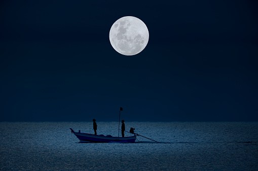 Full moon in the sky with silhouettes people on boat in water at night.
