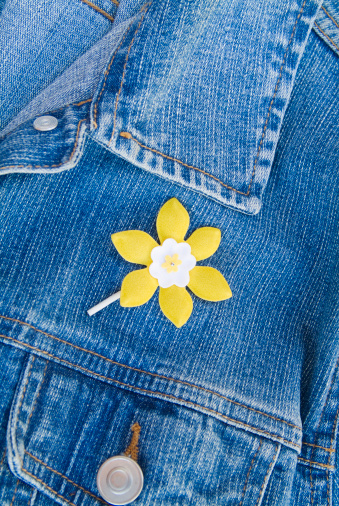 A daffodil lapel pin on a denim jacket.  Symbolizes the fight against cancer. 