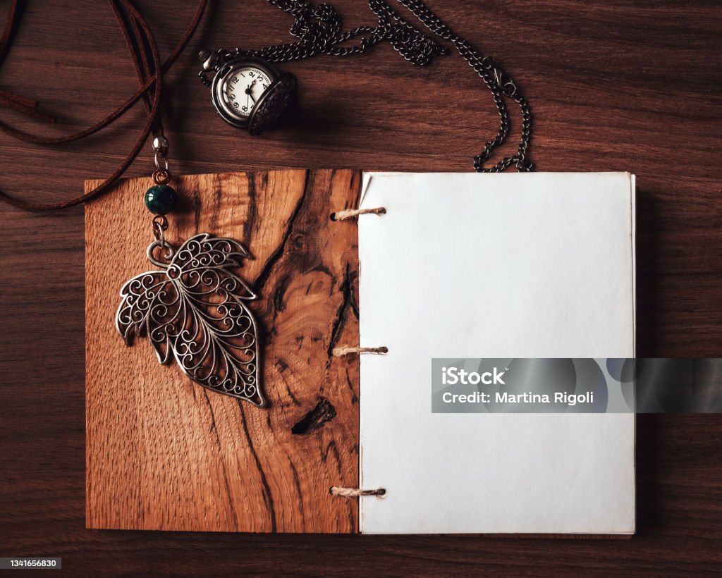 Blank diary page with leaf pendant and pocket watch on wooden background, flat lay Flat Lay Stock Photo
