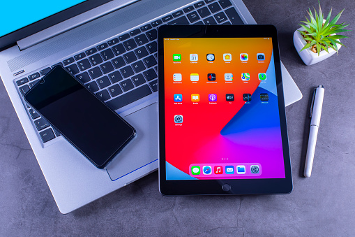 Galati, Romania, March 31, 2021: - Apple release new iPad 8th generation with the powerful A12 Bionic chip, support for Apple Pencil and the smart keyboard. iPad 8th generation with smartphone over silver laptop on desk.